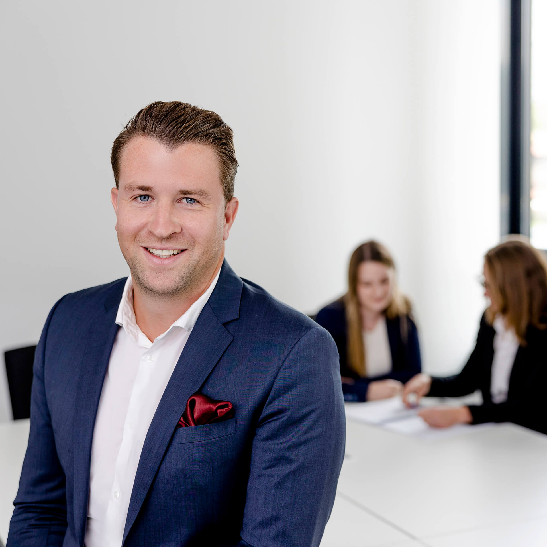 Ein Datenschutz-Jurist von activeMind.legal lächelt in die Kamera, während hinter ihm weitere Mitarbeiter der Kanzlei an einem Fall arbeiten